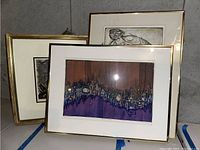 Three framed wall art pieces leaning against a wall, various sizes, showing different styles including abstract cityscape and sketches