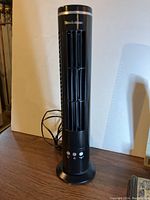 Brookstone mini tower fan standing on table with power cord extended, front view showing fan vents and control buttons.