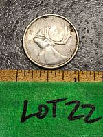 Obverse side of the 1961 Canadian 25 cent coin showing a caribou and the date 1961 on textured background with a ruler for scale.
