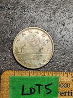 Top side of the 1966 Canadian silver dollar coin showing the Voyageur canoe design with two paddlers and a fur cargo. Includes inscriptions 'CANADA', '1966', and 'DOLLAR'. Ruler scale shown for size reference.