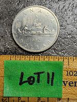 Reverse side of the 1982 Canadian silver dollar coin showing Voyageur canoe design with two figures and tree, including year and inscriptions.