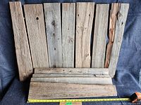 Overview of 11 assorted vintage barn boards arranged on a fabric surface showing size reference with a measuring tape highlighting the length about 29 inches