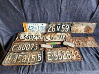 Photo of eleven Ontario license plates from 1940s, 1950s, and 1960s arranged on dark fabric showing various conditions and license numbers.
