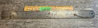 Full view of the steel ruler laid flat showing length markings and intact structure with rust and wear.