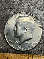 Photo of the obverse side of the coin showing the profile of John F. Kennedy, inscriptions, and the dual date 1776-1976. Coin surface shows wear and tarnish.
