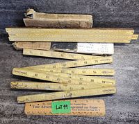 Photo showing vintage slide rule with printed measurement scales and large folding ruler in a worn cardboard box, displaying aged and dirty condition