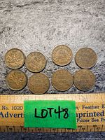 Eight Canadian one cent coins arranged on a textured surface with visible ruler for scale showing their size. Coins exhibit wear and oxidation.