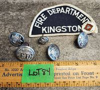 Photo of the fabric patch with 'Fire Department Kingston' text and six metal firefighter buttons displayed on a surface with a ruler for scale.