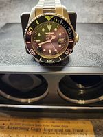 Front view of Invicta automatic wristwatch on black case background showing black dial, luminous markers, date magnifier and rotating bezel.