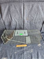 Full view of the rectangular metal live trap cage with wire mesh sides and solid metal base and top plate with handle.