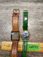 Pair of men's watches side by side on gray stone surface with ruler for scale