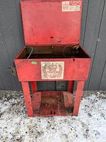 Front view of the red Citation parts washer showing the open top and metal grate inside basin on rusted legs.