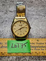 Front view of heavily worn Seiko Quartz watch with gold-tone metal bracelet and dial showing day and date.
