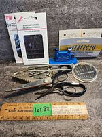Overview of the lot showing the large and small shears, needle threader, packs of needles, and safety pins arranged on a grey surface with a wooden ruler for scale.