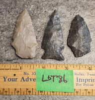 Three stone arrowheads placed on a grey textured surface next to a ruler for scale. They range from about 2.75 to 3.5 inches in length.