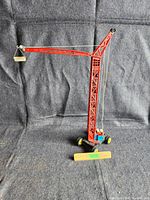 Full view of the red tin toy crane with extended boom and small bucket attached by wire, showing overall structure and scale with a ruler.
