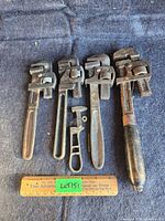 Four vintage adjustable wrenches laid out on blue cloth with a ruler for scale, showing length from 10'' to 14''