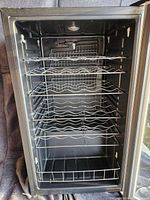 Front-open view of the Igloo wine cooler showing black interior with metal wine racks and dirty surfaces.