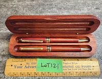 Top view of the open wooden case showing the pen and pencil inside resting on wooden inserts next to a ruler.