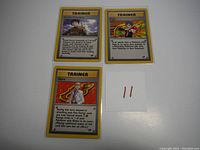 Photo of three Pokemon Trainer cards featuring Brock's Protection, Blaine, and another Trainer card