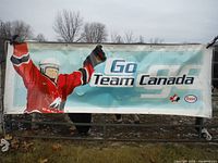 Front side of the large vinyl banner showing the ice hockey player graphic and 'Go Team Canada' text with Esso and Canadian Olympic Committee logos in outdoor setting.