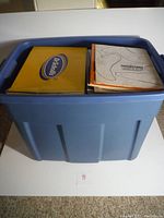 Blue plastic bin filled with various teddy bear making materials, papers and patterns on top.