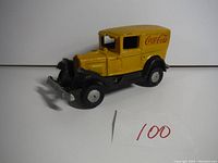 Front angle view of the yellow and black cast iron Coca-Cola truck showing front grille, bumper, wheels, and side door with Coca-Cola logo.
