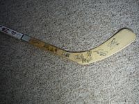 Full blade of hockey stick showing many player autographs on natural wood surface.