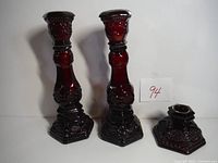 Two ruby red glass candlesticks placed side by side showing hexagonal bases and decorative embossed details.