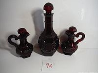 Front view of the three ruby red glass decanters set, showing the various sizes and stoppers
