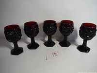 Front view of 5 ruby red goblets with embossed floral design and hexagonal stems, arranged in a row
