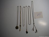Six vintage costume jewelry chains and necklaces laid flat on a surface with label '27'.
