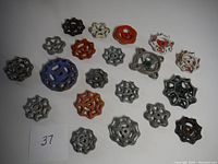 Overhead photo of 20 metal valve handles arranged on a white surface in a group showing variety of sizes and colors.