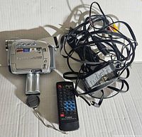 Silver Canon ZR65MC camcorder with charger, remote control, extra battery, and cables laid out on cardboard surface.