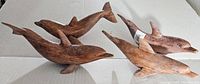 Four hand carved wood dolphins displayed together showing natural wood finish and smooth texture.