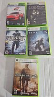 Five Xbox 360 video game cases arranged with cover art visible.