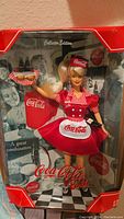Front view of Barbie Coca Cola Waitress Doll in original box showing doll in red and white uniform, tray, and vintage Coca Cola background.