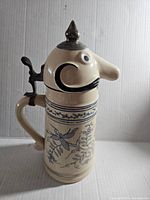 Side view of full stein showing character head lid, handle, and blue floral body design.