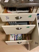 Four white drawers partially open, showing organization and contents related to kitchen utensils and supplies.