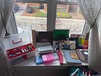 Overall view of art supplies kit on a window sill with various items and storage totes