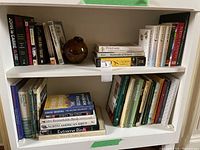 Books arranged on shelves and stacked, titles visible include works by John le Carré, Hillary Rodham Clinton, Toni Morrison, Bram Stoker and Jane Austen.