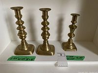 Set of three brass candle sticks of different heights displayed side by side with size notes visible