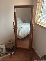Front view of full-length standing cheval mirror in bedroom showing wooden frame and base supports