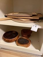 Shelf with stacked wood cutting boards, pizza peel, and vintage wood placemats.