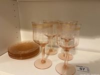 4 pink Depression glass wine glasses and 5 matching plates displayed on a shelf with visible gold trim and etched patterns.