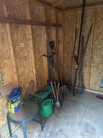 View of garden tools, shovels, watering can, and patio table in shed corner
