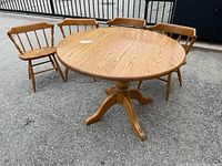 Photo showing round oak pedestal dining table and four oak spindle back chairs on a paved surface.