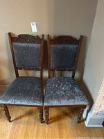 Front view of two wooden dining chairs with decorative carved tops and crushed velvet upholstered seats and backs.