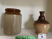 Photo showing both pottery items side by side on a shelf with a label indicating dimensions and lot number.