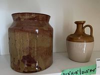 Photo showing brown glazed pottery crock and smaller two-tone jug on white shelf